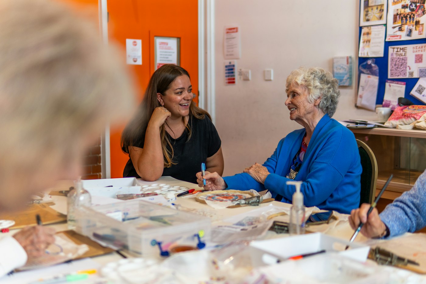 A caregiver laughing and talking with an older woman at a table