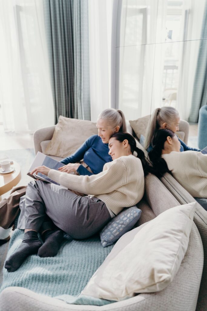 A grown daughter leaning on her mother as they look through a photo book together on the sofa