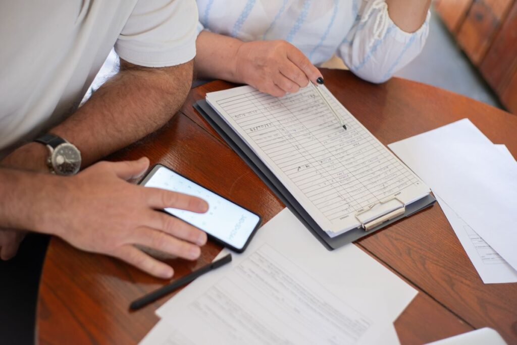 A couple going over bills and paperwork with a phone calculator at a wooden table