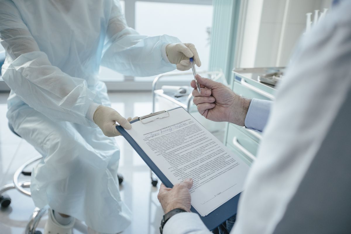 A clinician holding out a pen and a clipboard of forms for a patient to sign