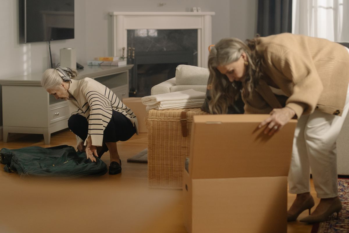 Two women sorting belongings and packing moving boxes in a living room