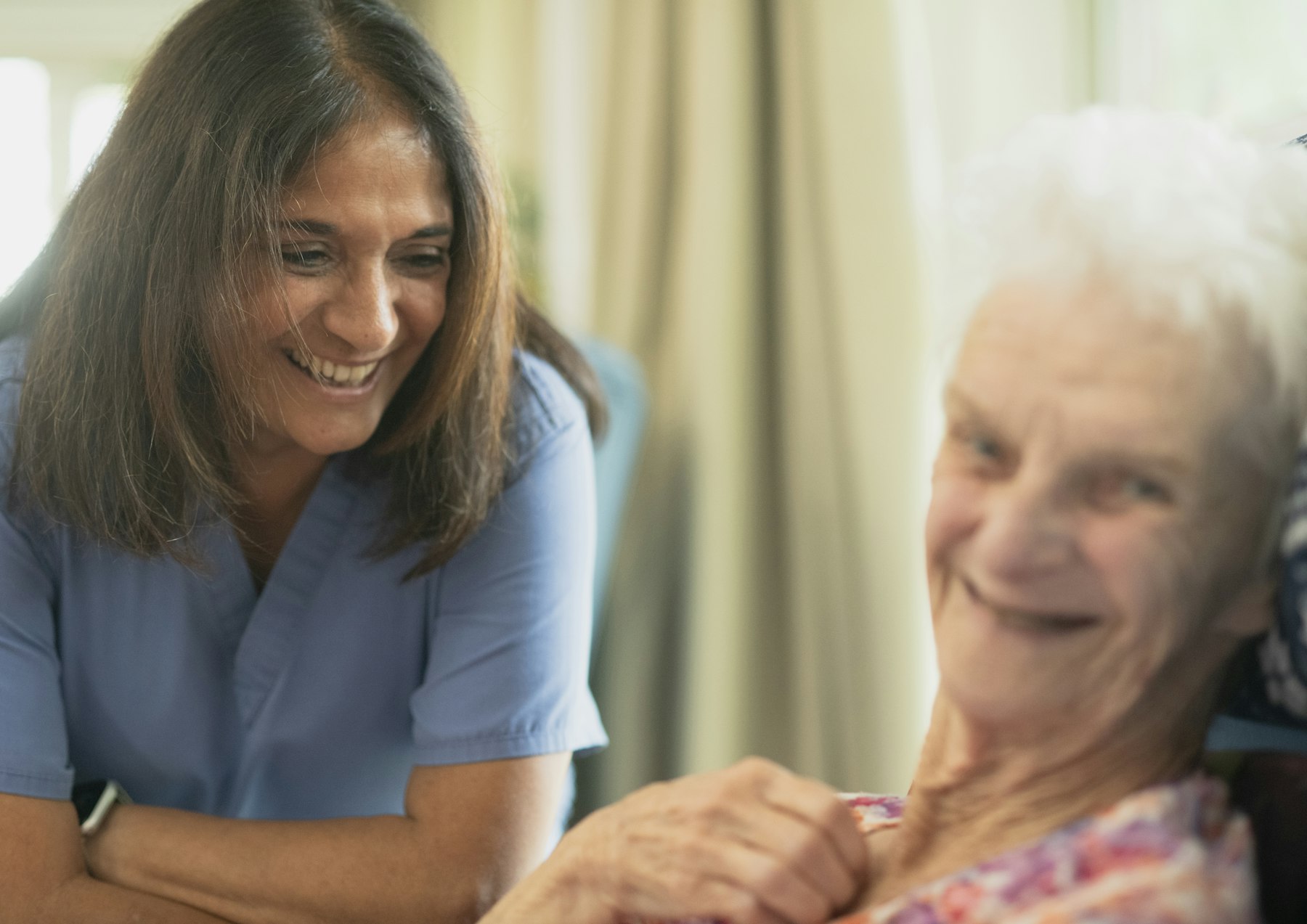 A smiling nurse leaning in to talk with a senior