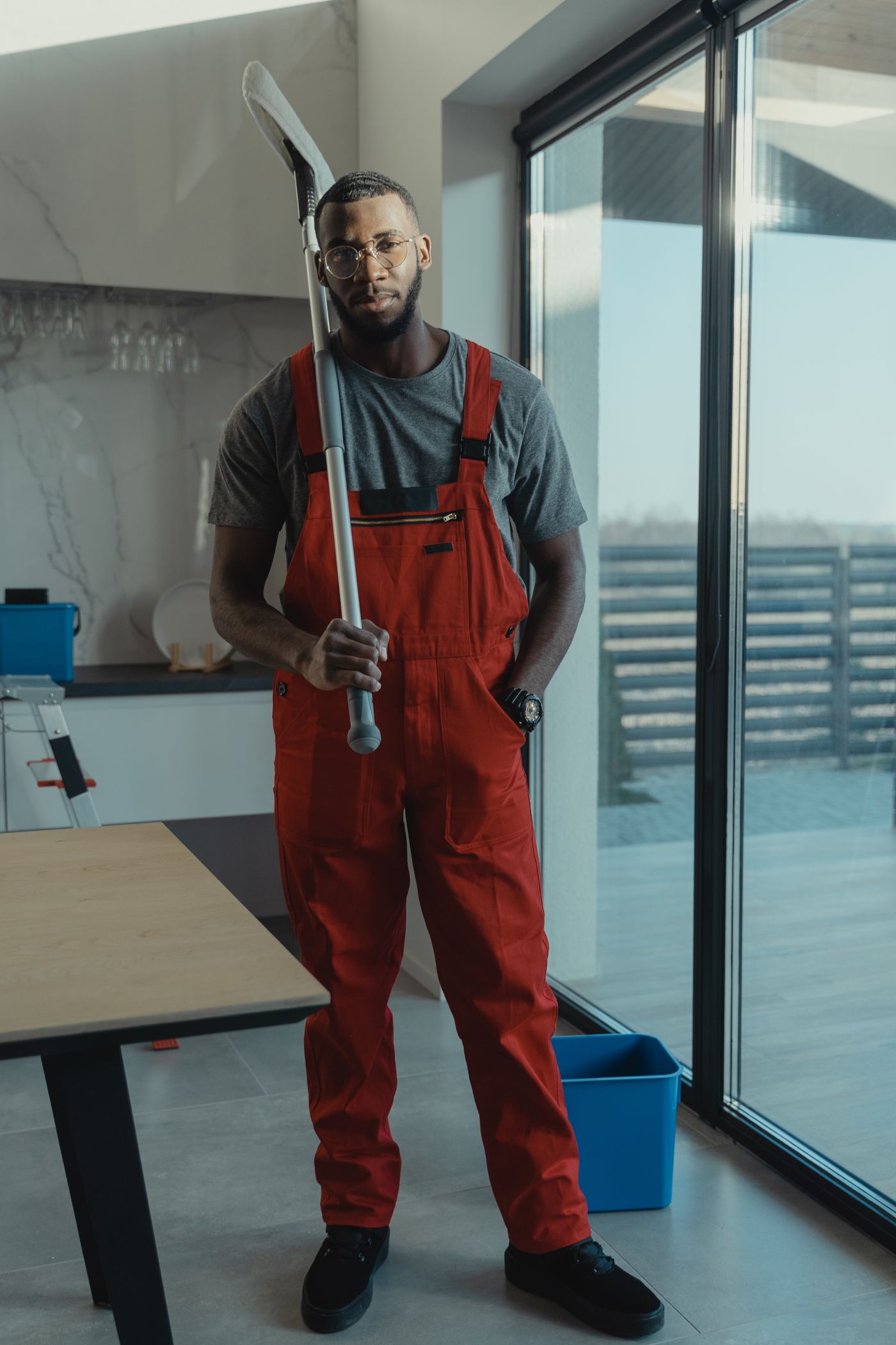 A cleaning professional in red work overalls holding a floor mop